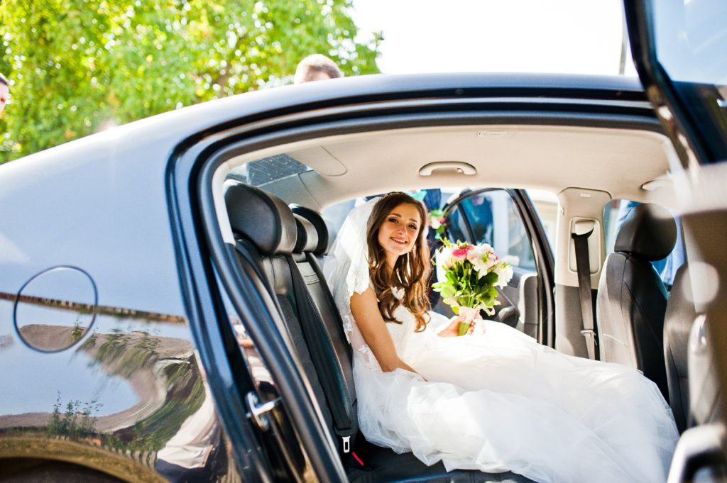Cute little bride sitting at car and looking at camera at sunny day